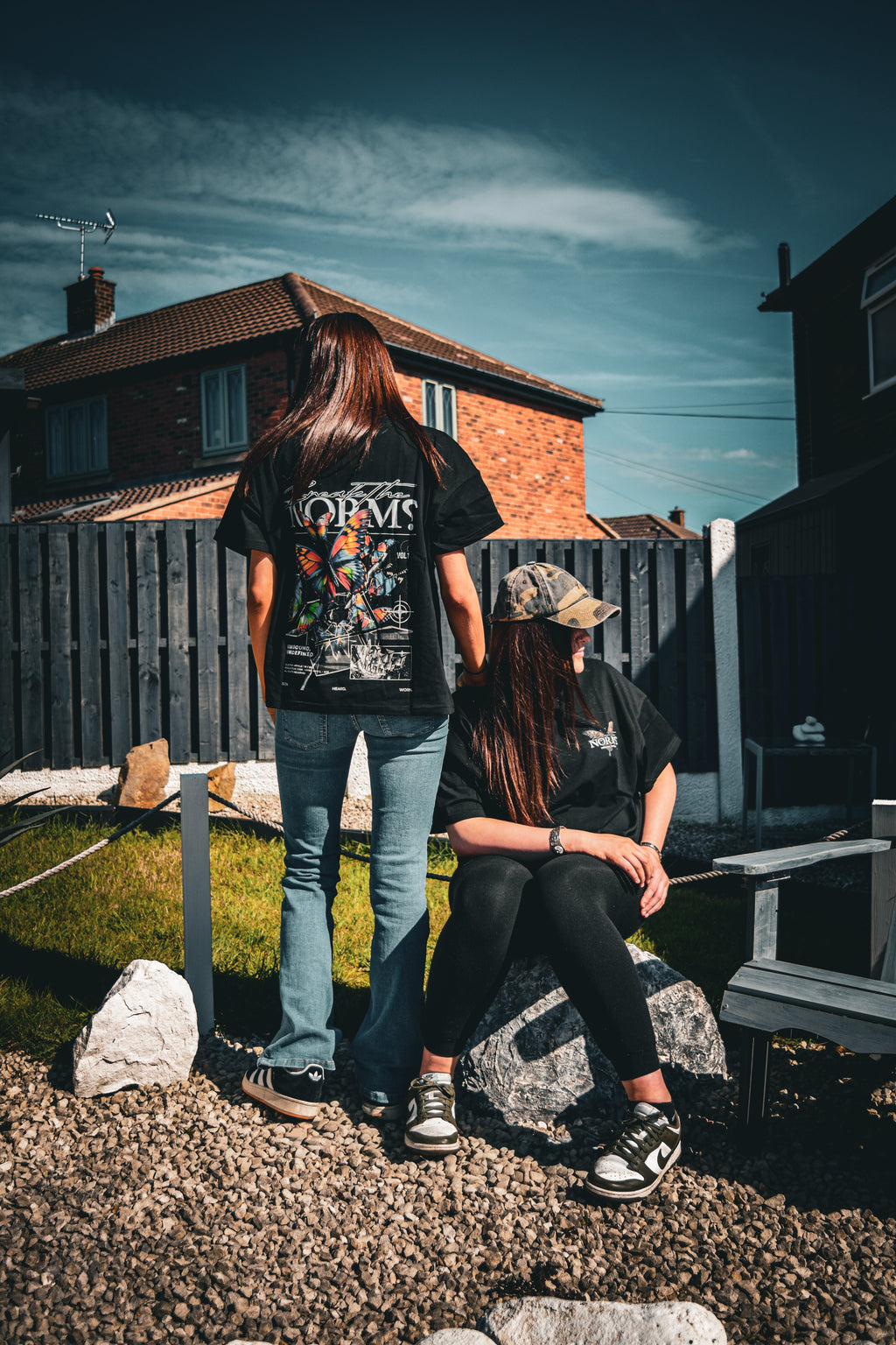 Two women wearing NORM CLOTHING black heavyweight cotton cropped t-shirts with graphic butterfly prints outdoors.
